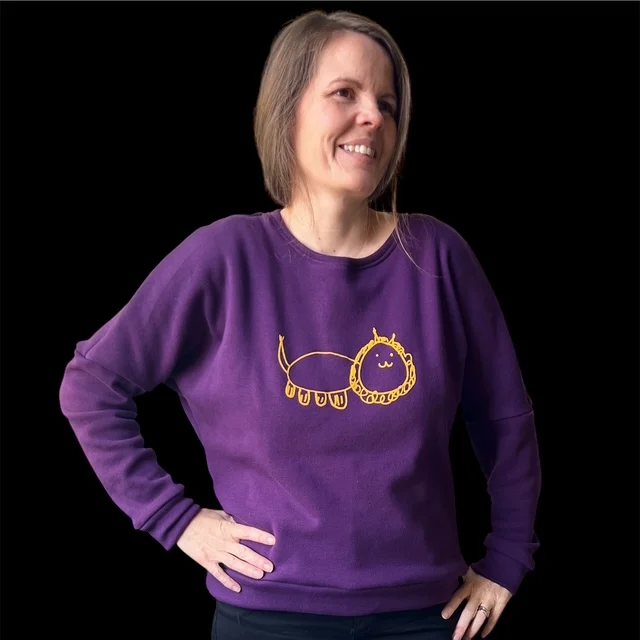 Romi trägt einen violetten Pullover mit der gelben Löwenzeichnung ihrer Tochter